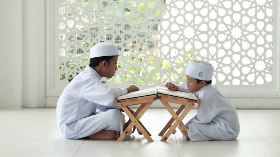 Dua anak berpeci putih mengaji di depan rehal