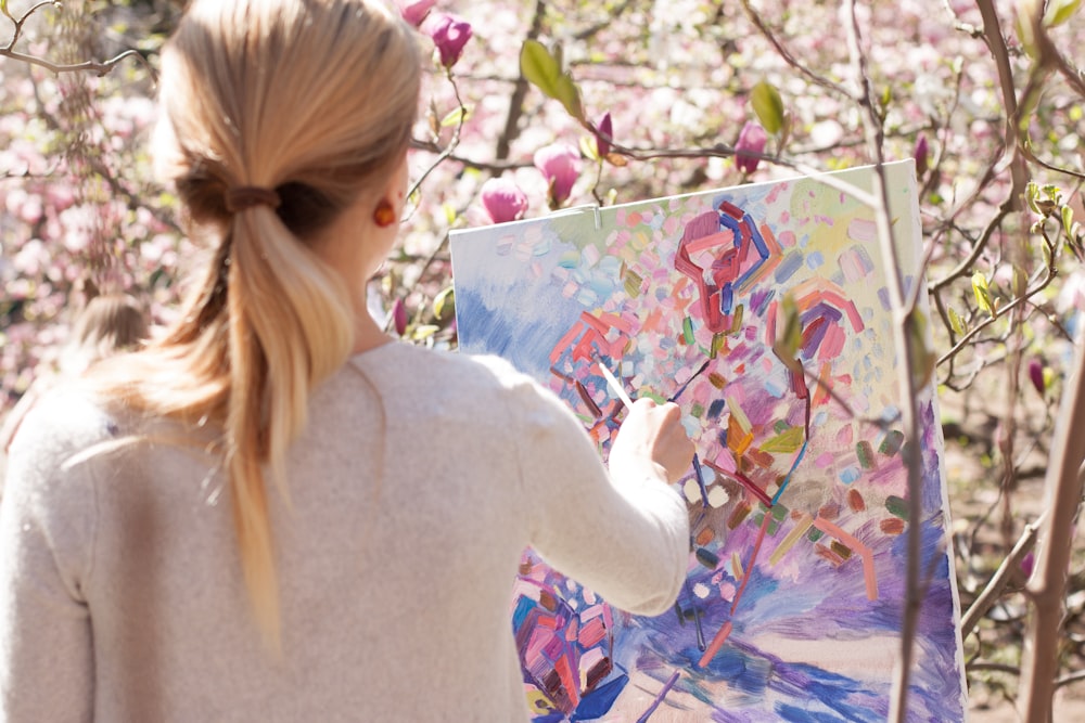 woman in white long sleeve shirt holding white and blue floral painting