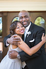 man in black suit hugging woman in white sleeveless dress