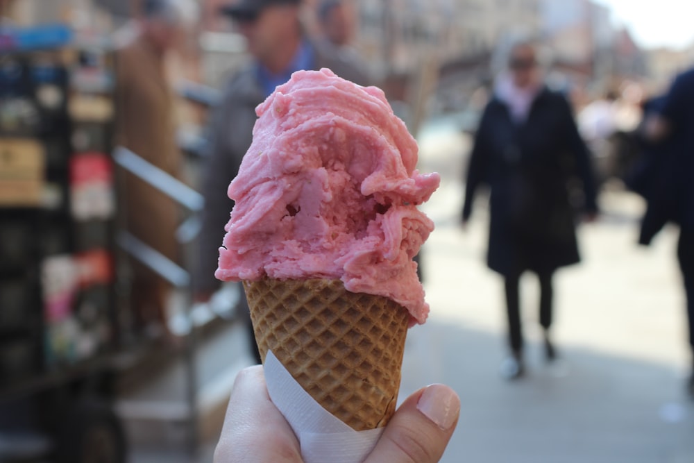 person holding ice cream cone with pink ice cream