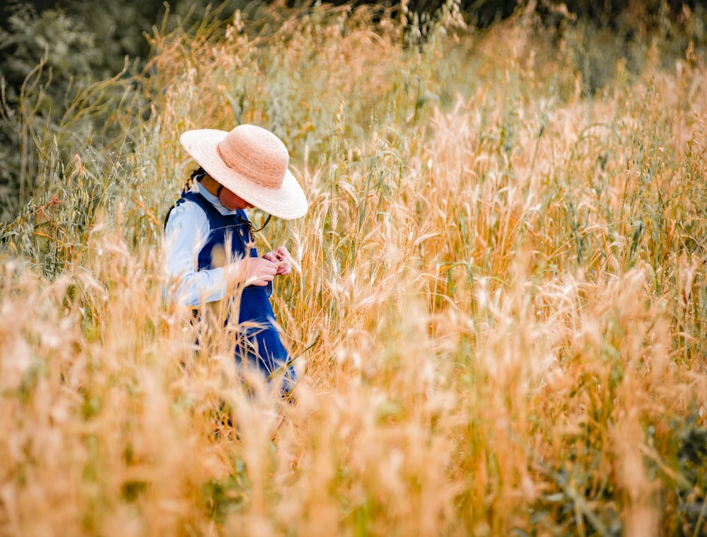 Femme en jean bleu et chapeau de paille marron assise sur un champ d’herbe brune pendant la journée