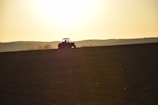 Sunset view of a tractor towing a plow across a freshly tilled field.