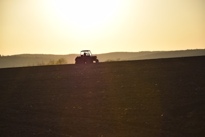 Sunset view of a tractor towing a plow across a freshly tilled field.