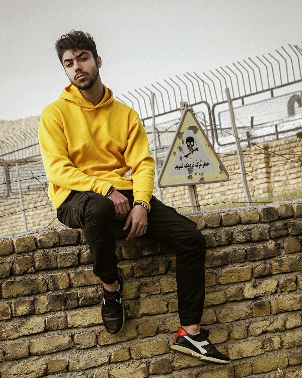 man in yellow hoodie sitting on gray concrete wall