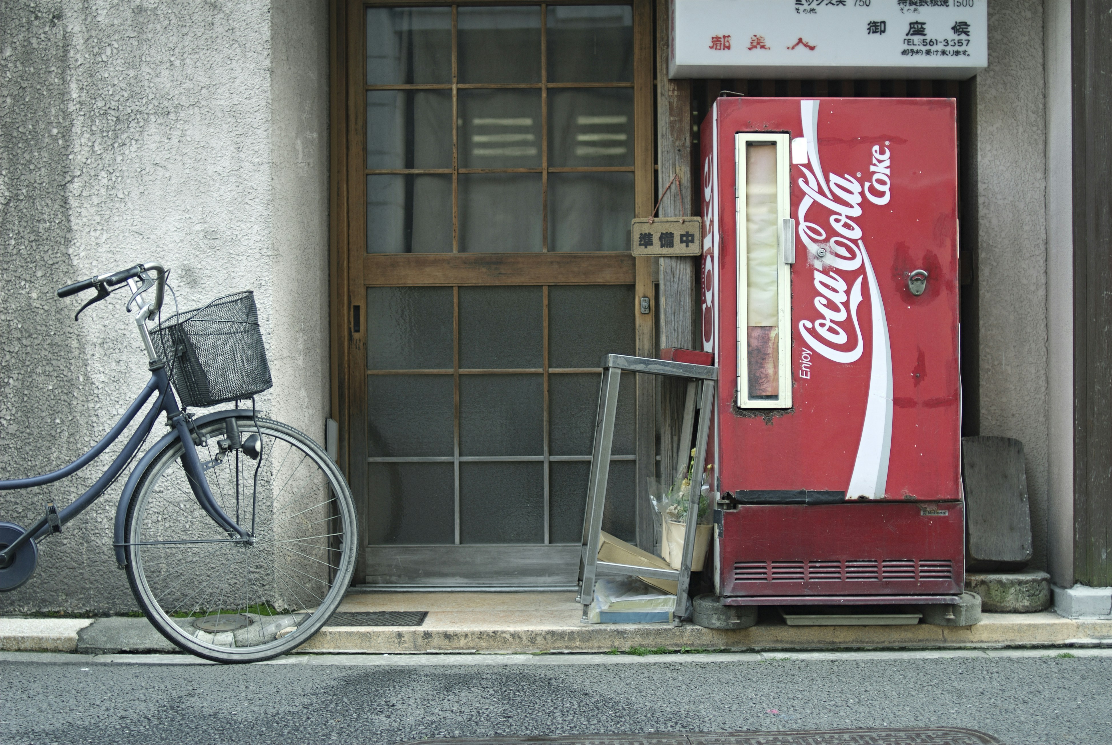 A bike standing by the wall, next to an old Coca-Cola machine.