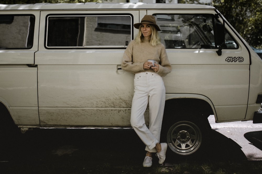 Femme en chemise à manches longues beige et pantalon blanc assise sur une voiture blanche