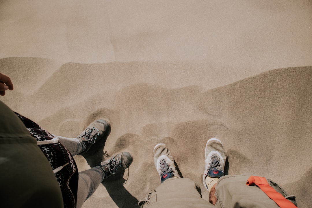 person in white pants and white sneakers standing on brown sand