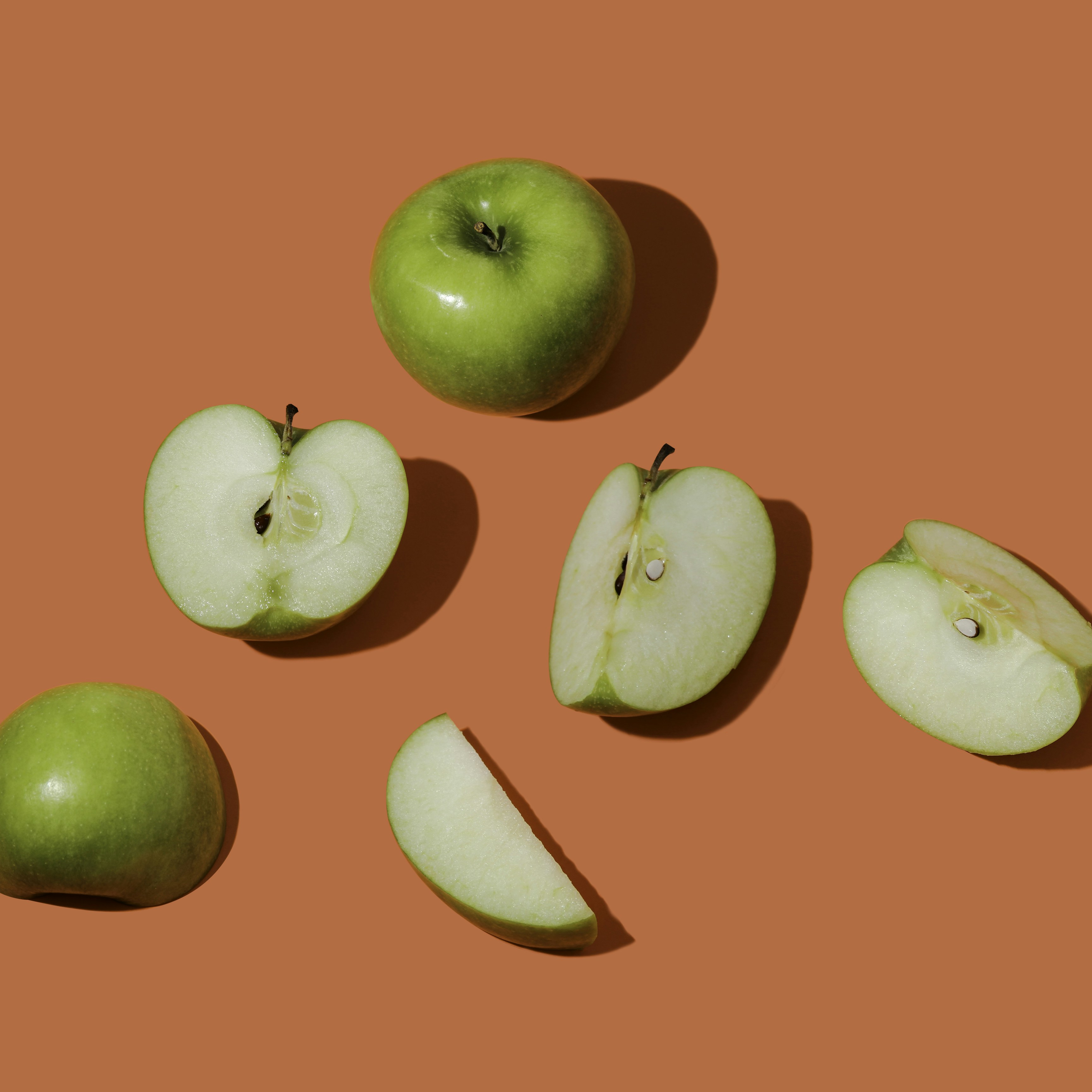 Green apples cut in various ways laying on an bright orange surface
