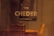 The image features the word 'CHEDER' in large, bold letters on a blurry background. Above it is a smaller text written in Hebrew. The setting appears to be indoors with warm lighting, and there’s a vague outline of furniture, such as chairs, in the background.