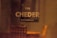 The image features the word 'CHEDER' in large, bold letters on a blurry background. Above it is a smaller text written in Hebrew. The setting appears to be indoors with warm lighting, and there’s a vague outline of furniture, such as chairs, in the background.