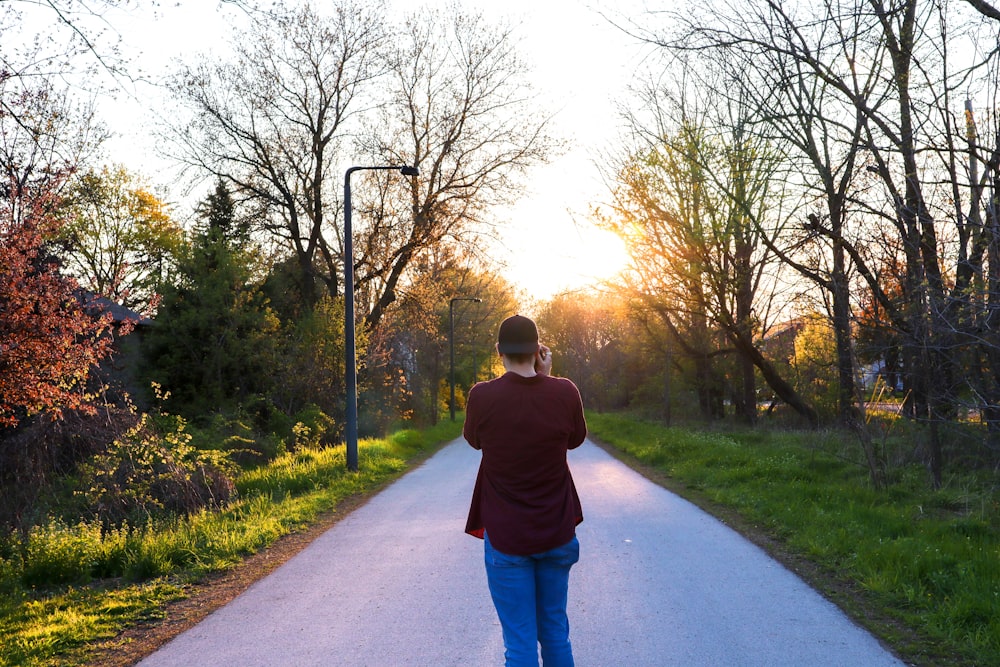 man in brown hoodie and blue denim jeans walking on gray concrete road during daytime