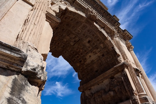 brown concrete building under blue sky during daytime in Arch of Titus Italy