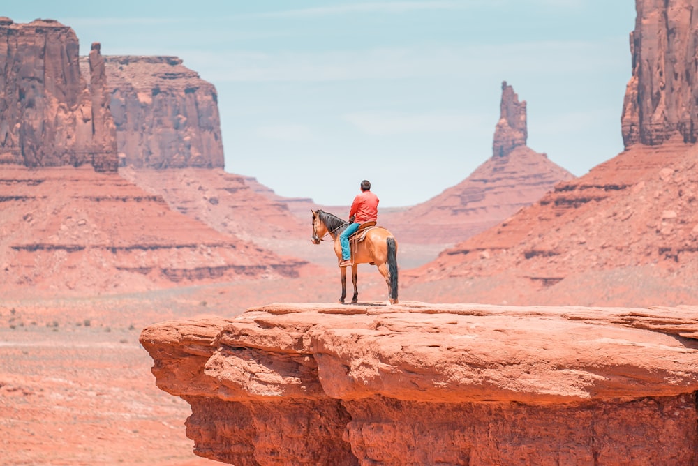 man in red jacket and black pants standing on brown rock formation during daytime