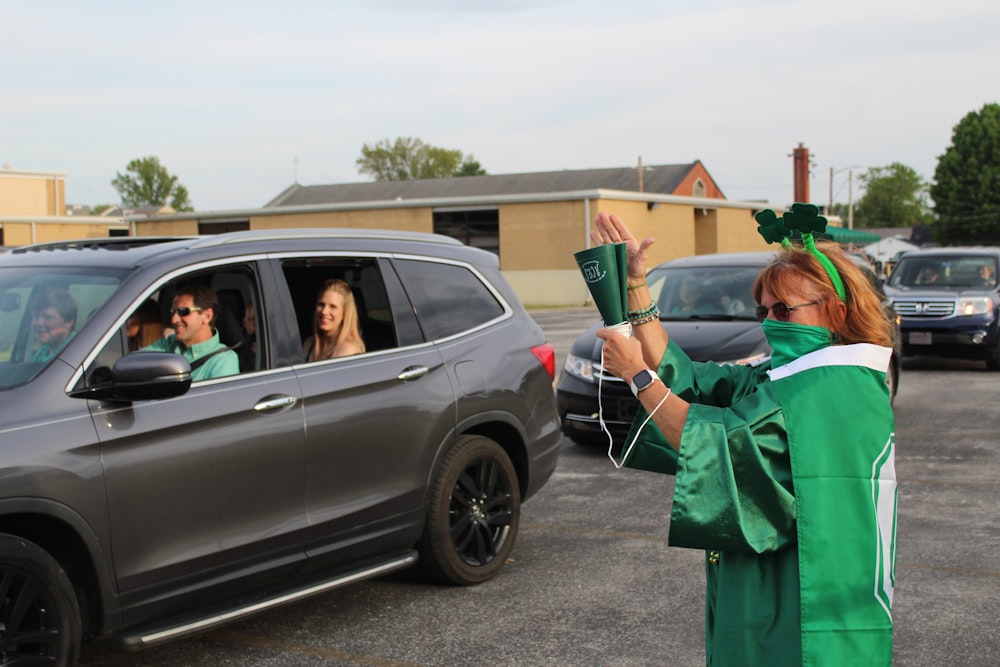 man in green robe standing beside gray suv during daytime