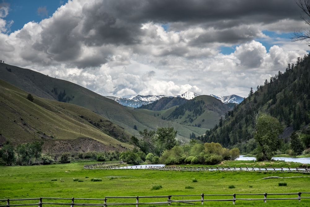 green grass field near green mountains under white clouds during daytime