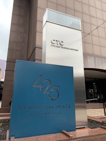A modern building exterior with signage for the Chicago Trading Company and 425 S Financial Place at Gateway Plaza. The structure features a reflective metallic sign tower with bold lettering. The area appears to be part of a commercial or financial district.