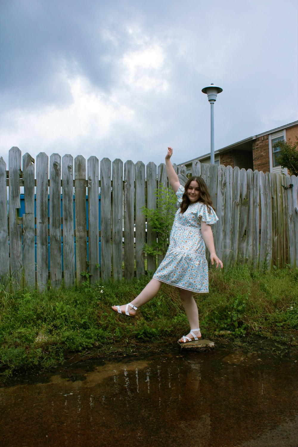 woman in blue dress standing beside wooden fence