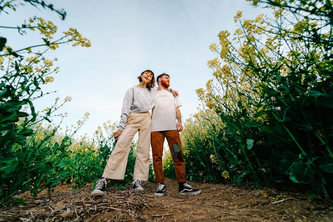 man and woman standing on brown dirt road between green plants under white clouds during daytime
