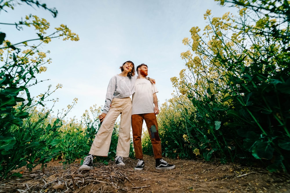 man and woman standing on brown dirt road between green plants under white clouds during daytime