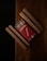 A red box of wooden matches is partially open, revealing a row of matchsticks inside. It is placed on a wooden surface with several wooden sticks arranged parallel and perpendicular to the box.