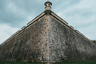 A towering walled city under a stormy sky, with faint silhouettes of otherworldly creatures lurking beyond the barriers.