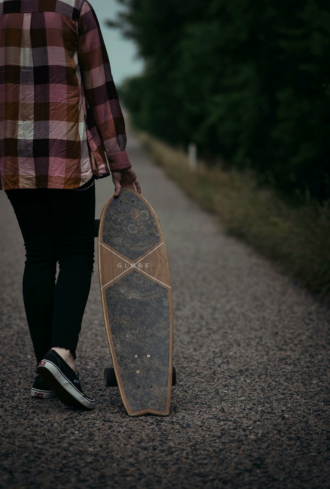 person in red and black plaid dress shirt and black pants holding brown and black skateboard