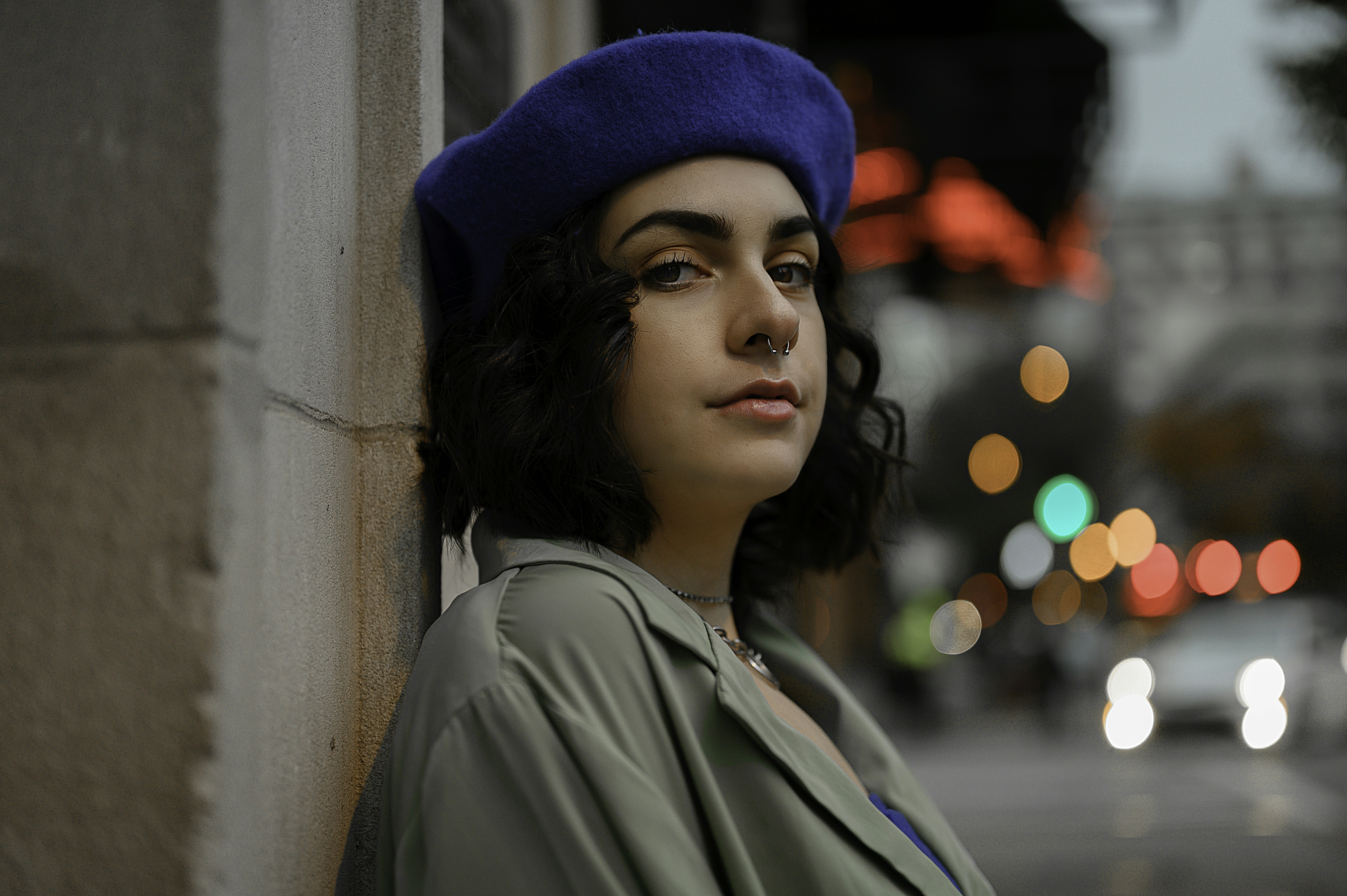 woman in blue knit cap and green jacket leaning on wall