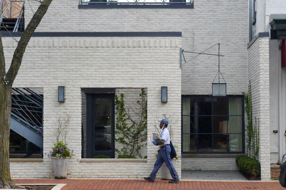 a man walking down a street past a white brick building
