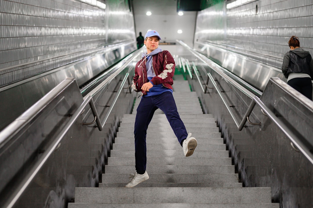 man in red jacket and blue denim jeans walking on gray concrete stairs