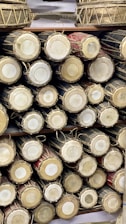 A collection of traditional drums is neatly arranged on shelves, showcasing the circular drumheads and intricate rope lacing. The drums vary in color, with natural wood and darker tones highlighted.