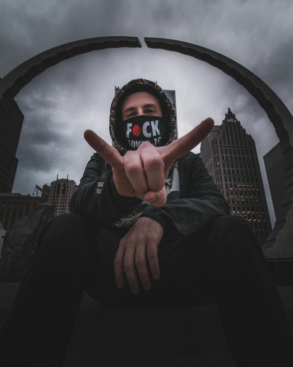 man in black jacket and black pants sitting on round concrete building during daytime