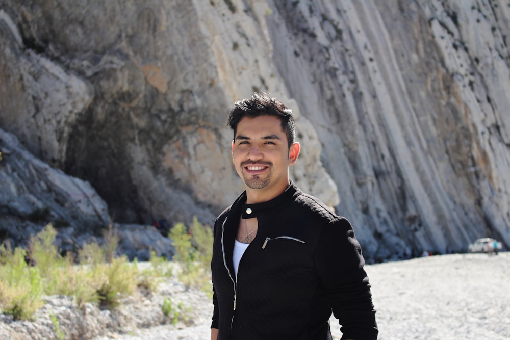 man in black jacket standing near gray rock formation during daytime