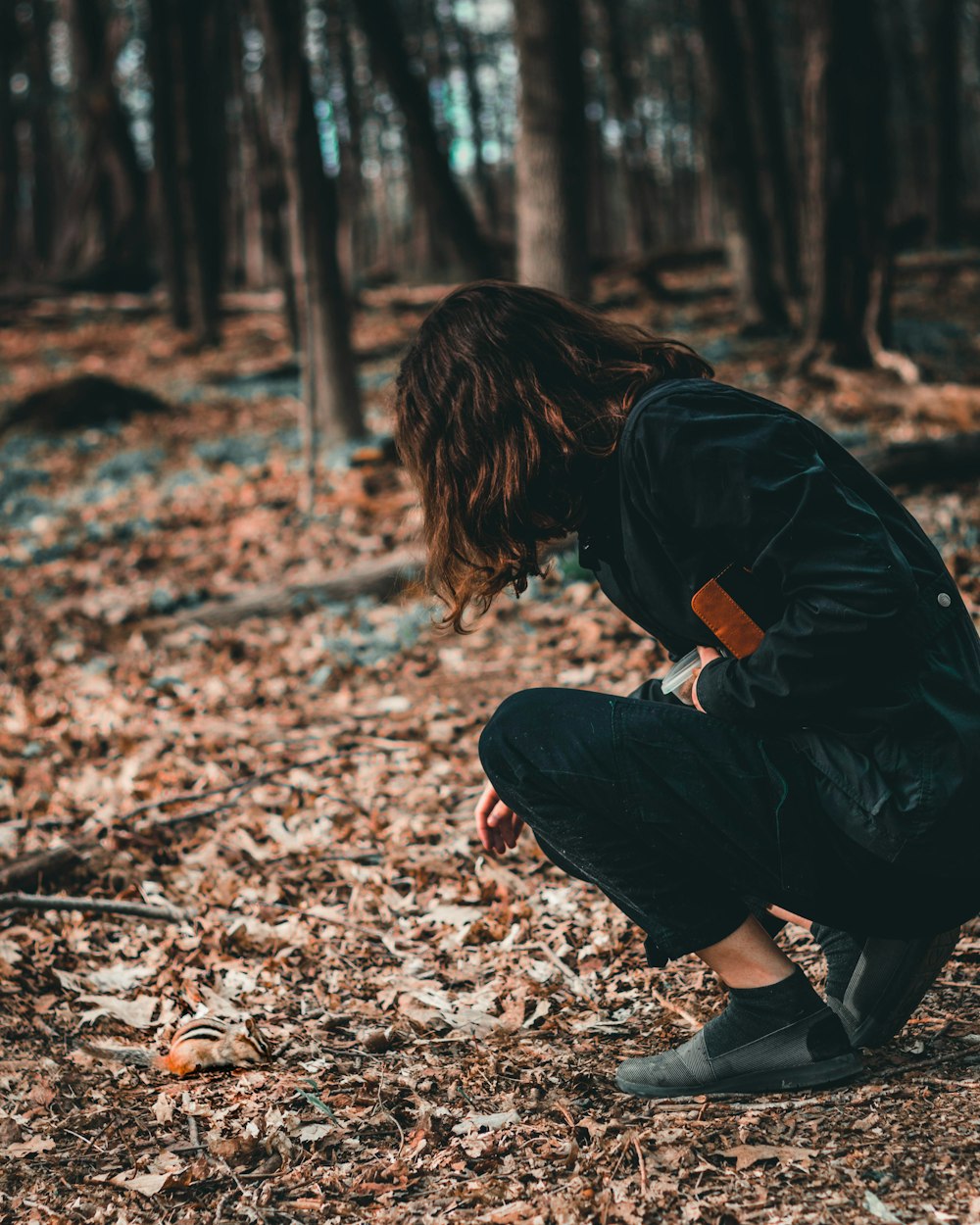 woman in black jacket and pants sitting on ground with dried leaves