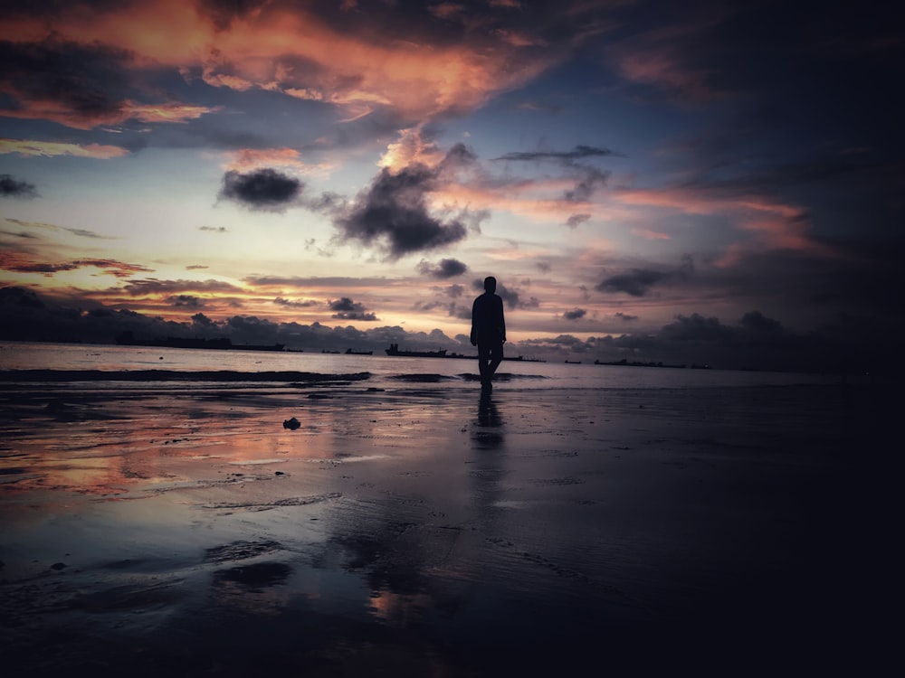 silhouette of person standing on seashore during sunset