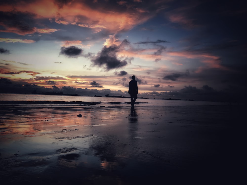Silhouette der Person, die während des Sonnenuntergangs am Meeresufer steht