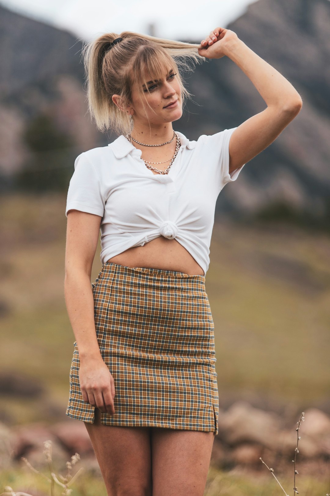 woman in white shirt and brown and black plaid skirt holding her hair