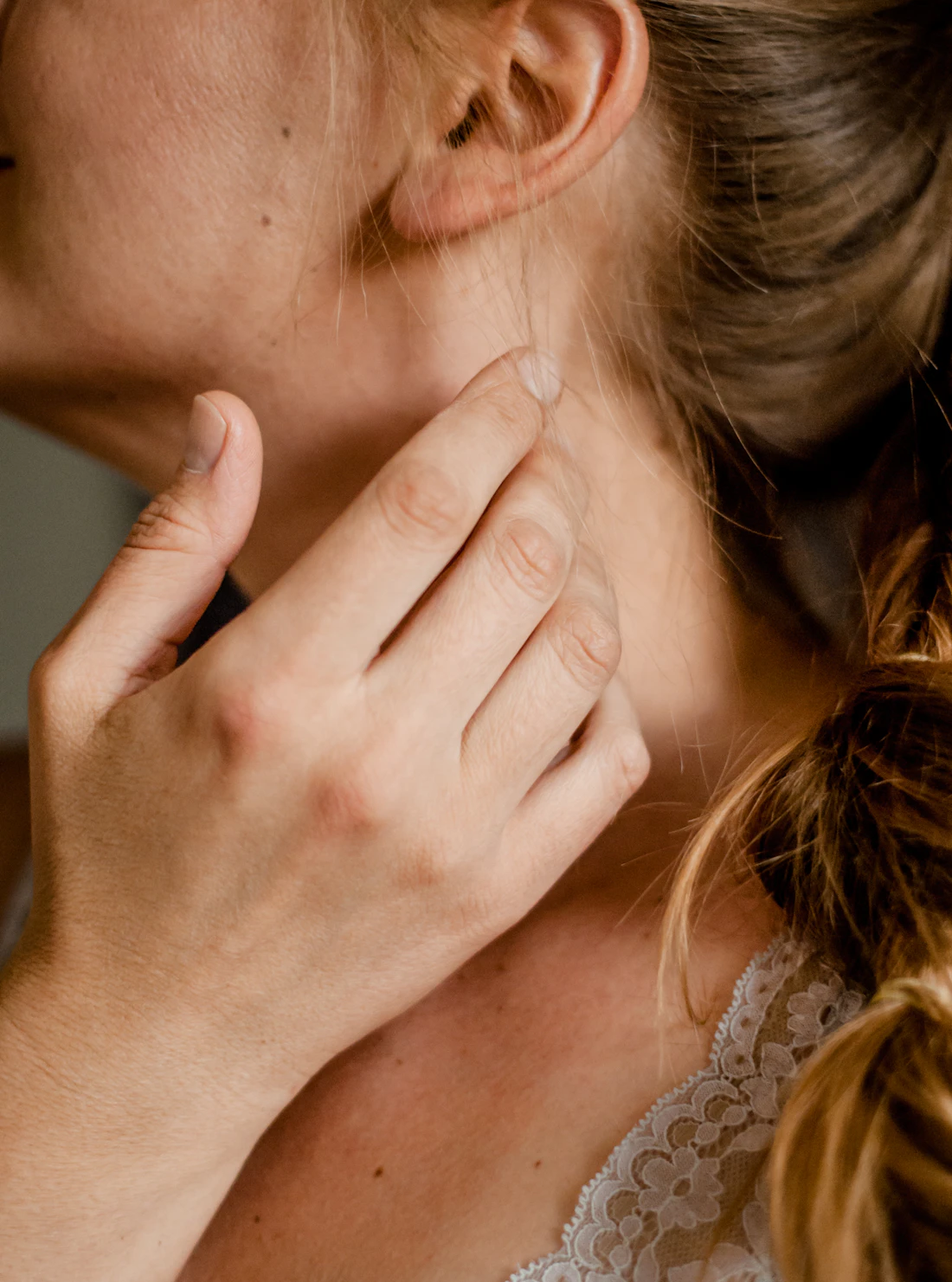 A woman's jaw, ear and neck seen from the side with a hand resting on her neck; her eyes are out of frame
