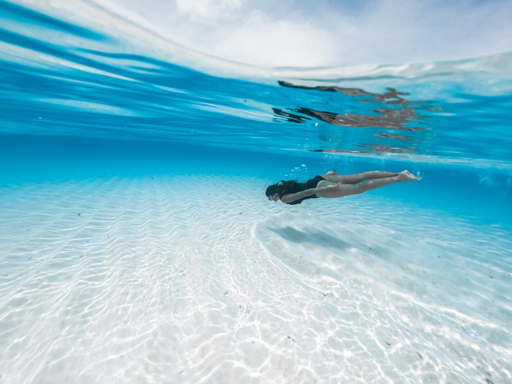 woman in black bikini lying on white sand beach during daytime