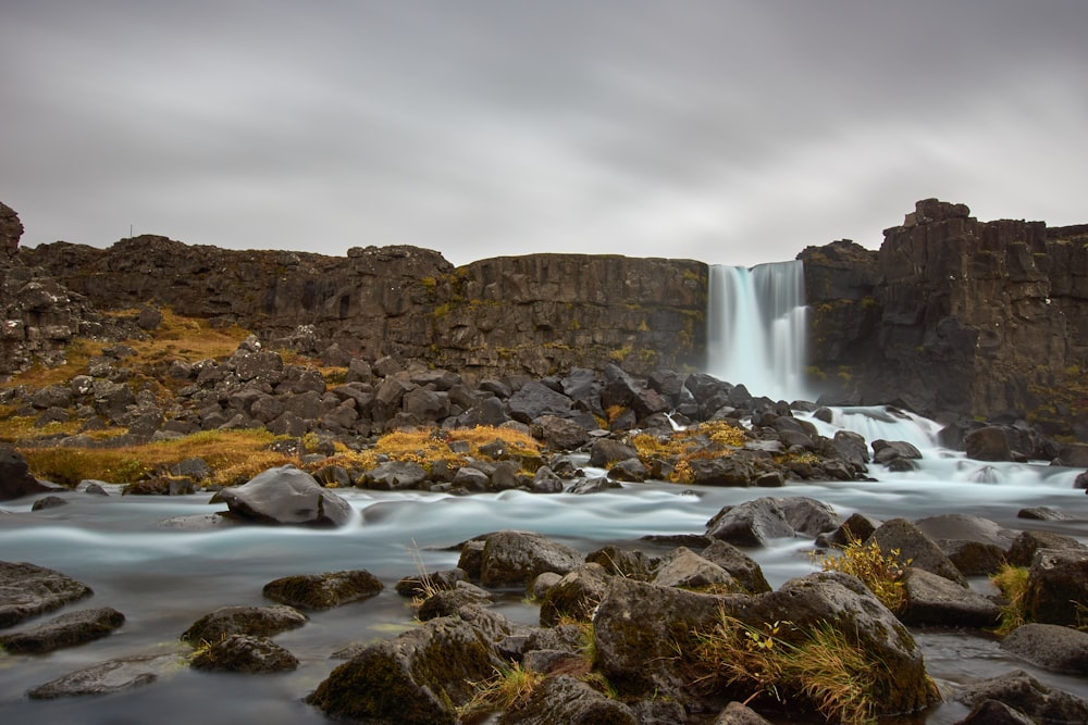 water falls on rocky mountain under cloudy sky during daytime