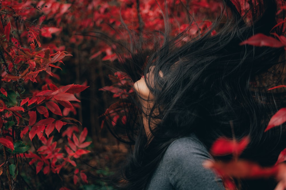 woman in gray sweater standing near red flowers