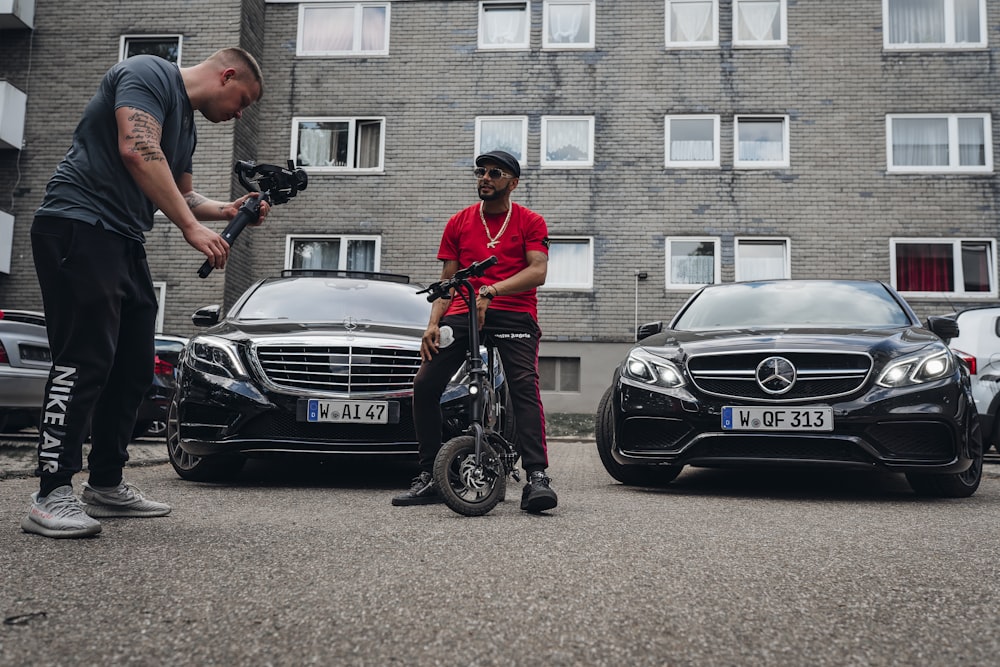 Homme en polo rouge et pantalon noir chevauchant une voiture Mercedes Benz noire