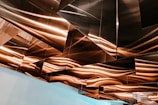 Geometric metal panels are installed on a ceiling, reflecting warm light and creating an abstract pattern with wavy lines.