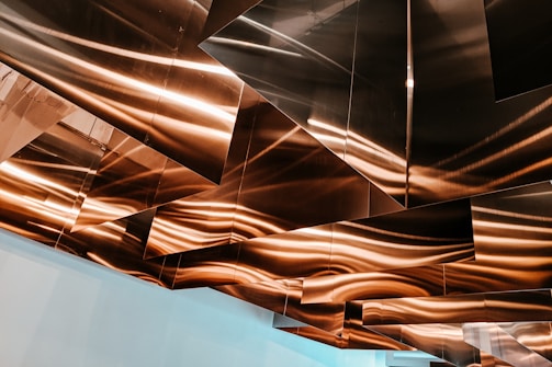 Geometric metal panels are installed on a ceiling, reflecting warm light and creating an abstract pattern with wavy lines.