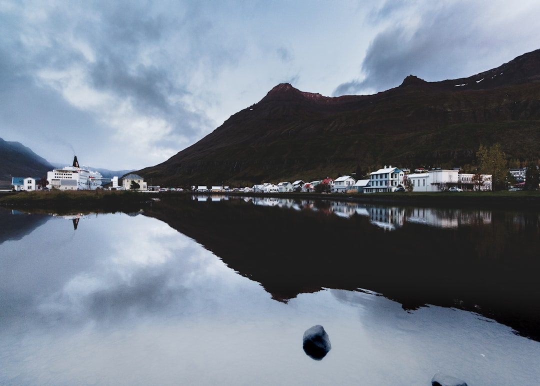 body of water near mountain under cloudy sky during daytime