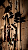 Various tools including a hammer, wrenches, and cables hang on a vertically striped surface. The light casts strong shadows, creating a dramatic effect with the tools silhouetted against the background.