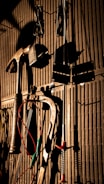 Various tools including a hammer, wrenches, and cables hang on a vertically striped surface. The light casts strong shadows, creating a dramatic effect with the tools silhouetted against the background.