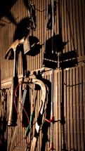 Various tools including a hammer, wrenches, and cables hang on a vertically striped surface. The light casts strong shadows, creating a dramatic effect with the tools silhouetted against the background.
