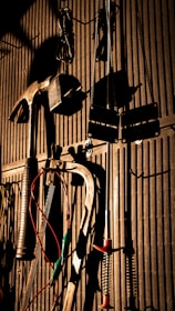 Various tools including a hammer, wrenches, and cables hang on a vertically striped surface. The light casts strong shadows, creating a dramatic effect with the tools silhouetted against the background.