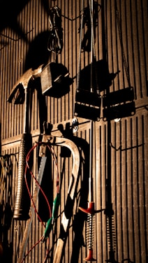 Various tools including a hammer, wrenches, and cables hang on a vertically striped surface. The light casts strong shadows, creating a dramatic effect with the tools silhouetted against the background.