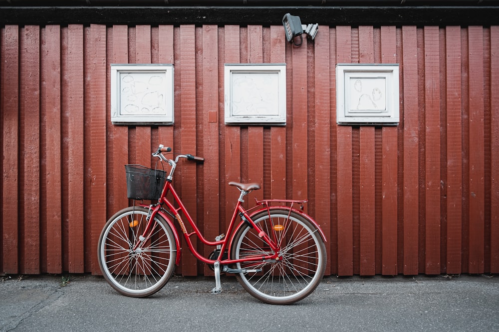 Bicicleta de ciudad roja estacionada junto a una pared de madera marrón